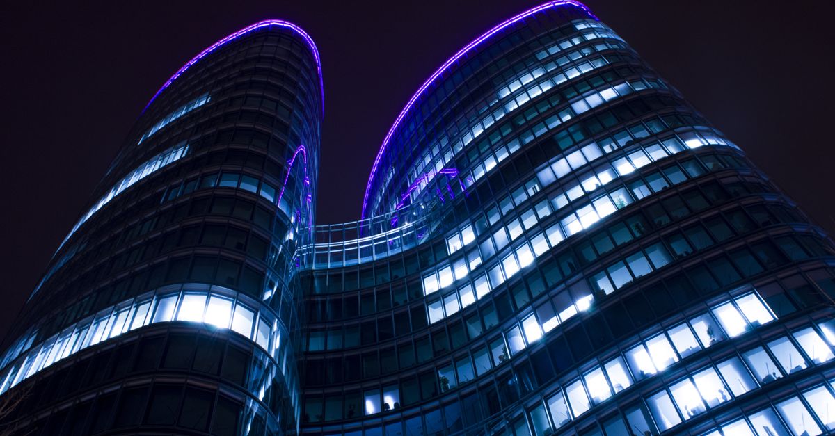Low angle view of a modern skyscraper with glowing lights and purple accents against a night sky.